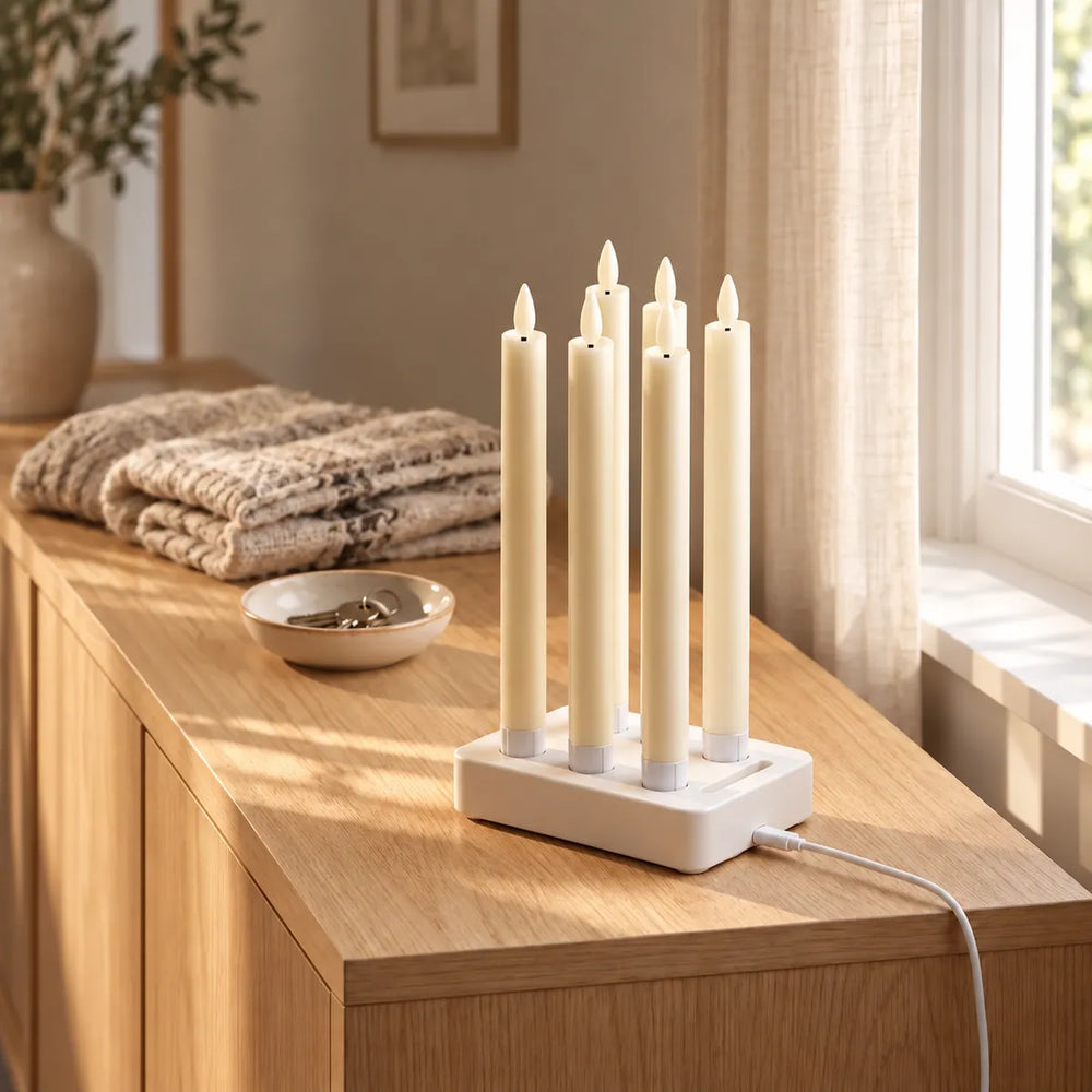 Six Wove Luma LED taper candles charging together in the white dock on an oak chest of drawers in morning sun