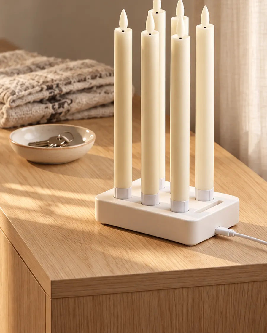 Six LED taper candles in the white charging dock on an oak chest of drawers in morning sun