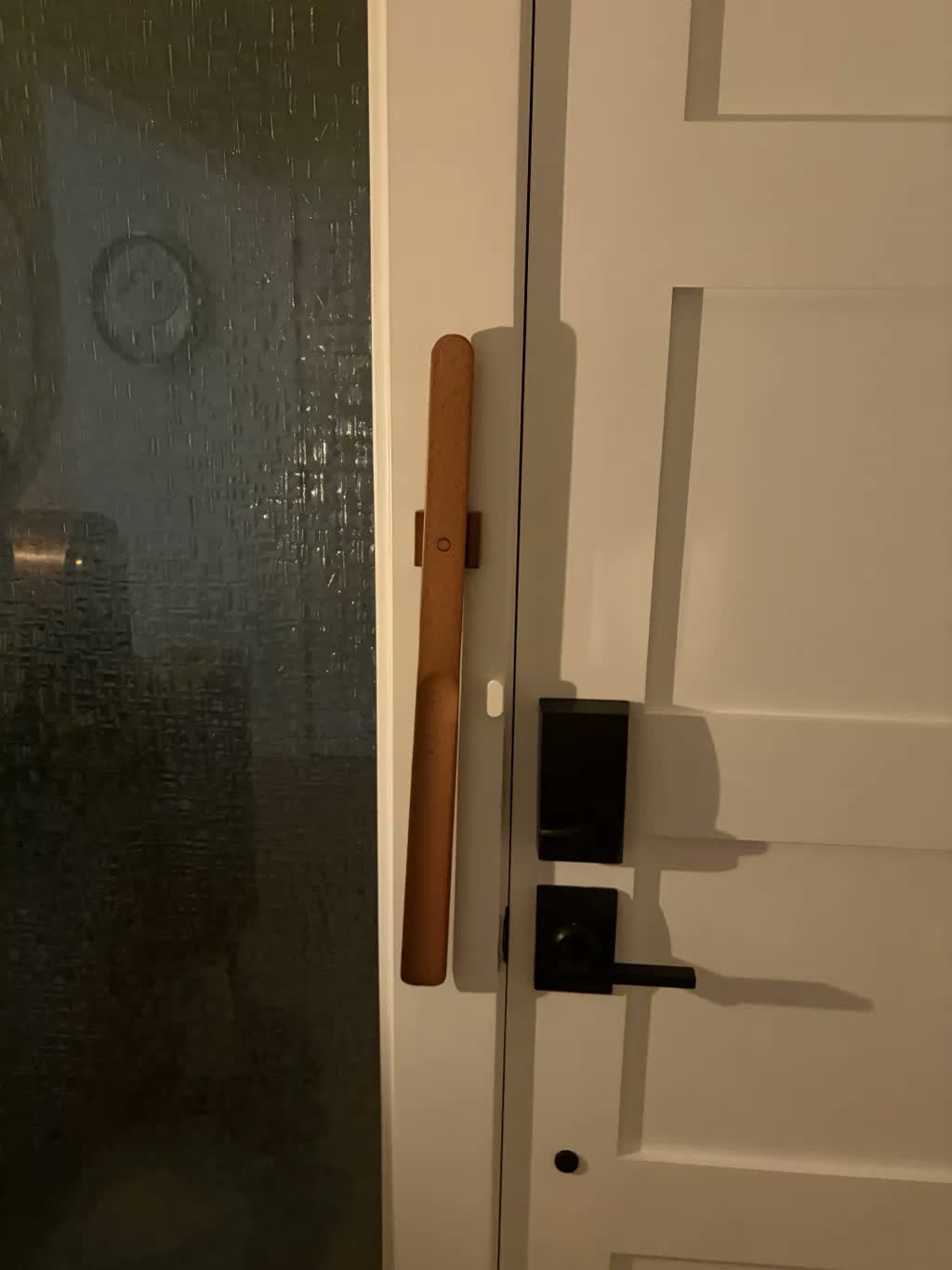 Light beech shoehorn magnet-mounted on a white door frame next to a black handle and smart lock