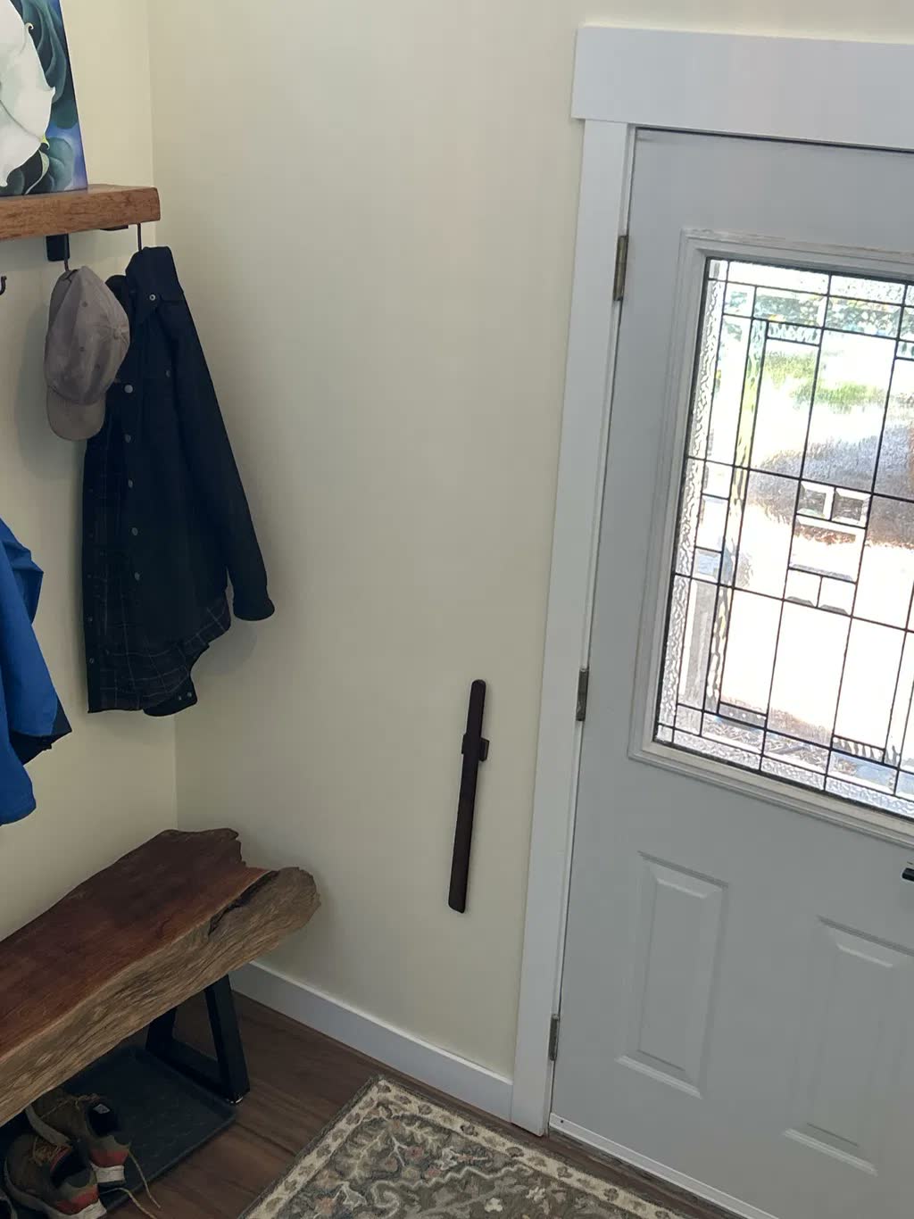 Dark walnut shoehorn on a cream boot room wall with a live-edge bench, coat hooks and a leaded-glass front door