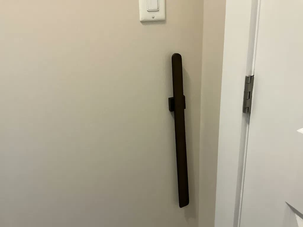 Near-black shoehorn on a beige wall beside a white door, with a light switch above it