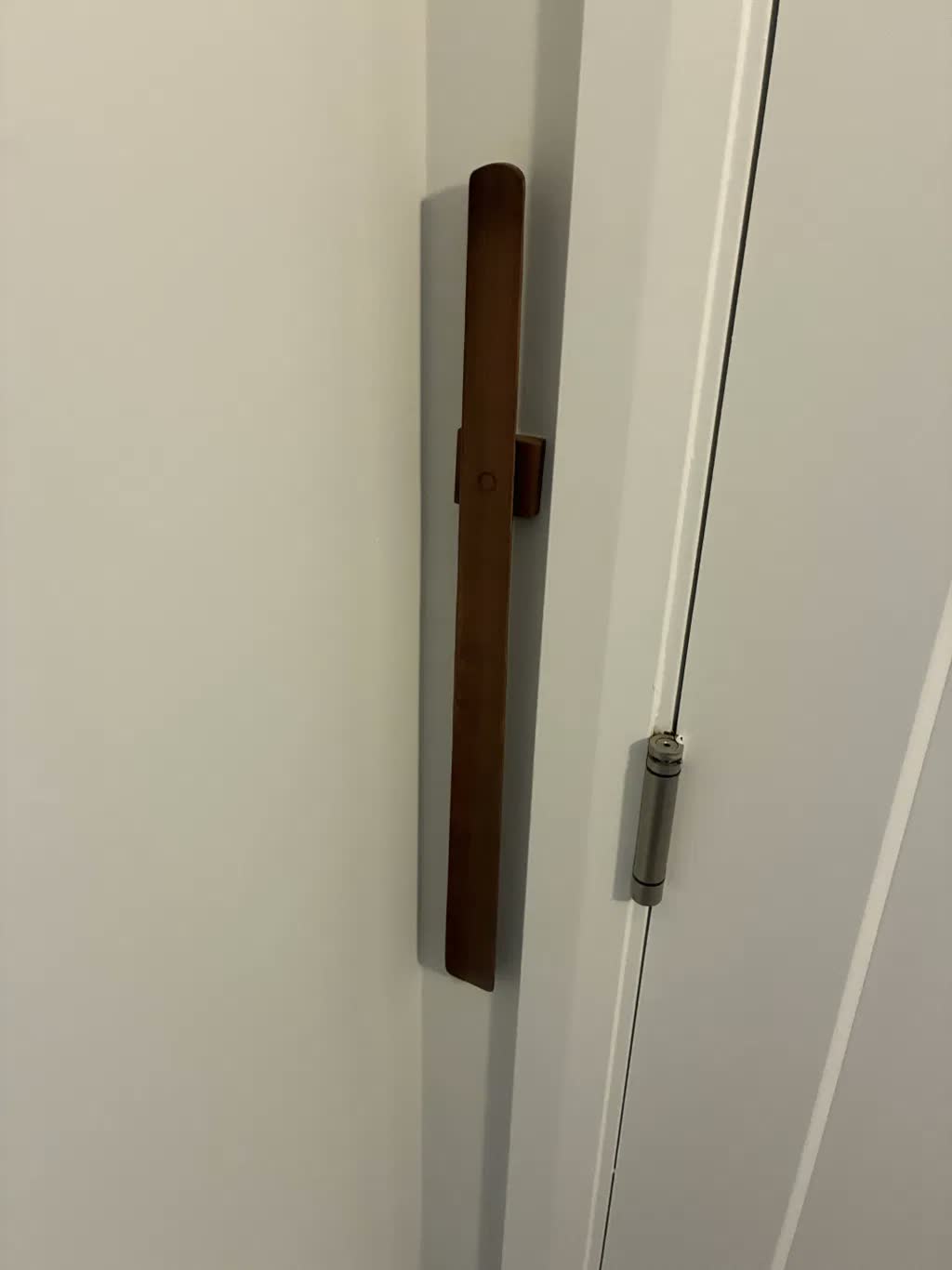 Close-up of a dark walnut shoehorn on a white wall beside a white door with a visible hinge