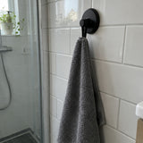 Matte black Wove hook on white tile with a grey towel