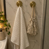 Two brushed gold Wove hooks on marble tile with a white towel
