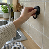 Hand pressing a black Wove hook onto beige kitchen tile